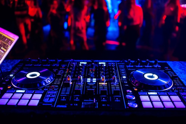 Controller musicale mixer dj in una discoteca a una festa sullo sfondo di sagome sfocate di persone che ballano