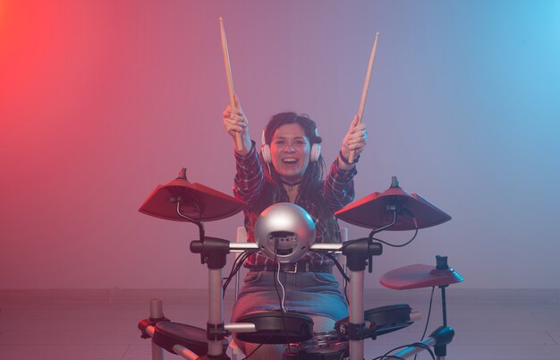 Music, drum and hobby concept - young woman playing the electronic drum set at the club