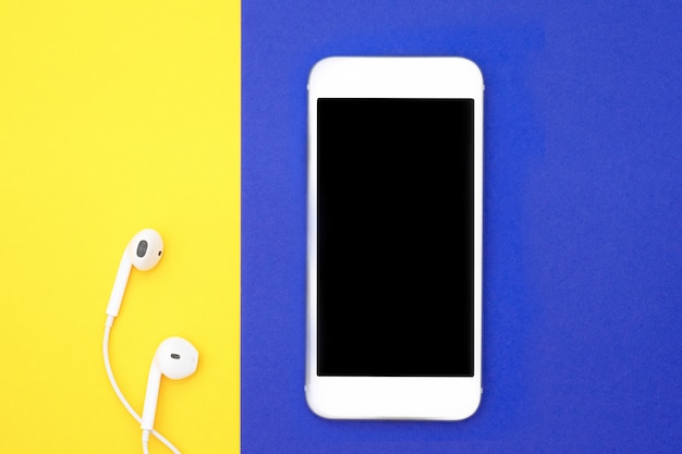 Music, gadgets, music lover. White smartphone and headphones on yellow and blue backgrounds with headphones