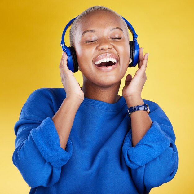 Music headphones and black woman singing in studio isolated on a yellow background podcast radio singer and happy african female streaming enjoying and listening to audio sound track or song