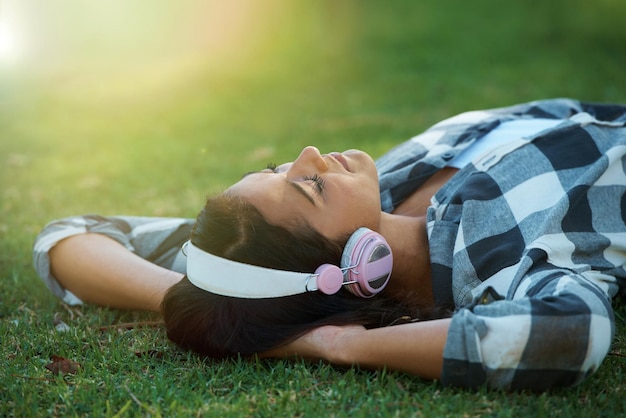 Photo music headphones park or woman on lawn to relax for rest in garden nature or field with smile or peace eyes closed streaming or calm person on break with playlist for radio or podcast on grass