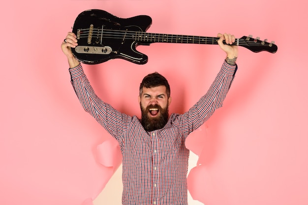 Music instrument guitarist through hole in pink paper holds\
guitar in hand bearded man guitarist