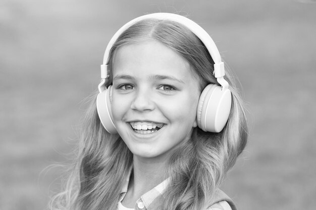 音楽は人生です幸せな子供は屋外で音楽を聴きます小さな女の子は音楽を演奏するヘッドフォンを着用します音楽レッスン新技術現代の生活楽しさと娯楽を聞いて学ぶ