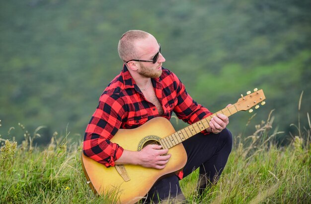音楽は、アコースティックギタープレーヤーのカントリーミュージックの歌のように聞こえるものです。市松模様のシャツのヒップスターファッションのギターを持つセクシーな男