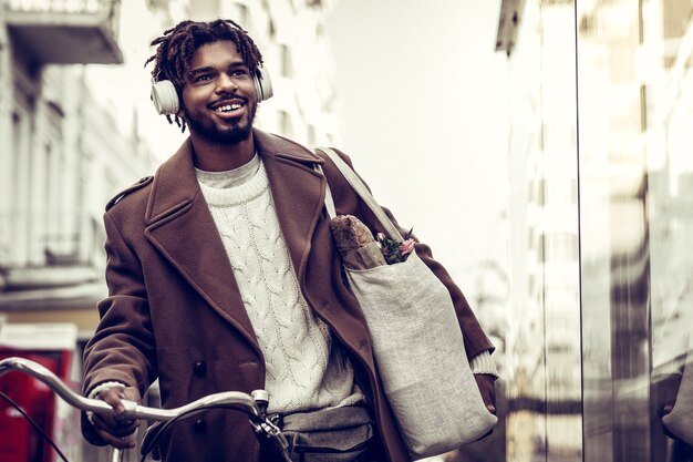 Music lover. Kind brunette man keeping smile on his face while walking in the street