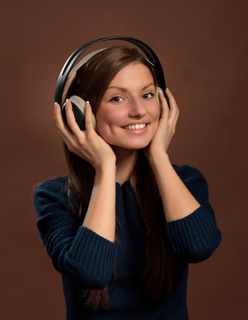 Photo music lover portrait of young smiling woman in headphones dark brown background