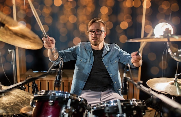 Photo music people musical instruments and entertainment concept male musician or drummer playing drums and cymbals at concert or studio over holidays lights background