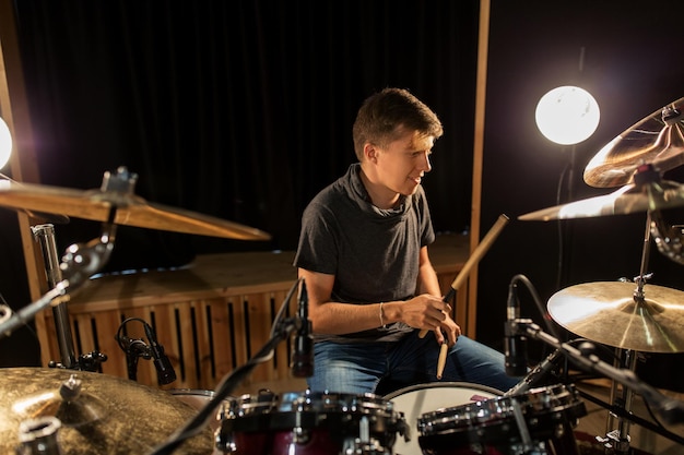 music, people, musical instruments and entertainment concept - male musician with drumsticks playing drums and cymbals at concert or studio