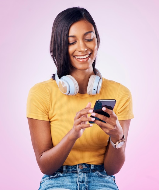 Music phone and Indian woman typing on pink background for social media website and chatting Relax happy and isolated girl streaming audio radio and track on smartphone for message on mobile app