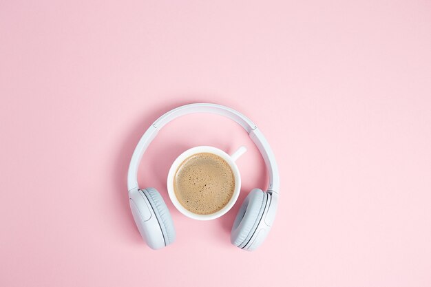 Концепция музыки или подкаста с наушниками и чашкой кофе на розовом столе. Вид сверху, плоская планировка