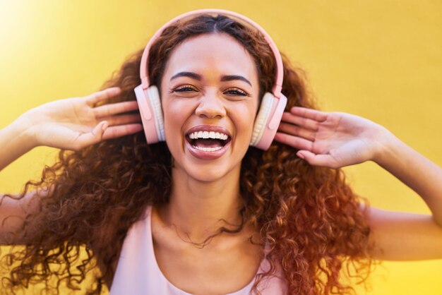 Foto ritratto musicale e libertà con una donna di colore che ascolta la radio all'aperto su uno sfondo di parete gialla