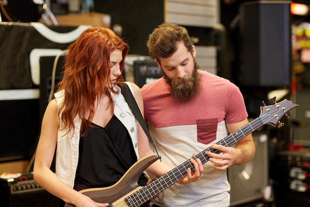 music, sale, people, musical instruments and entertainment concept - happy couple of musicians with bass guitar at music store