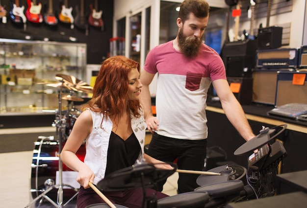 音楽、販売、人々、楽器、エンターテインメントのコンセプト-音楽店でドラムキットを持つ幸せな男と女