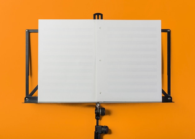 Music stand with blank white musical page on orange backdrop