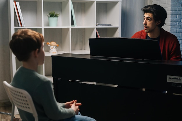 Music teacher explains to child student how to play piano and singing during lesson Musician male practicing piano lesson at home in living room Concept of music education