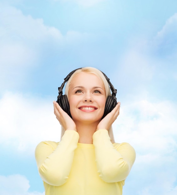 Music and technology concept - smiling young woman listening to music with headphones