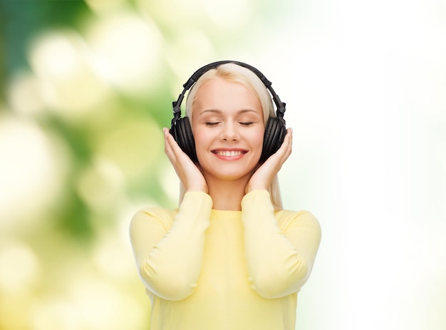 music and technology concept - smiling young woman with closed eyes listening to music with headphones