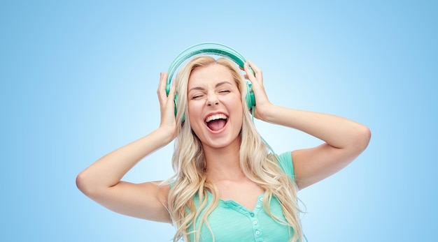 music, technology and people concept - happy young woman or teenage girl with headphones singing song over blue background