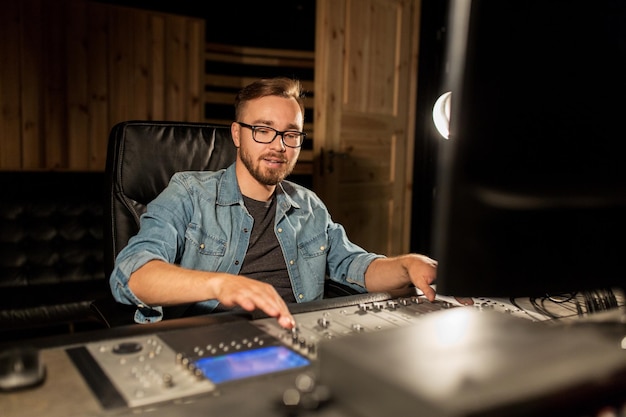 музыка, технология, люди и оборудование концепция - человек на микшерной консоли в студии звукозаписи