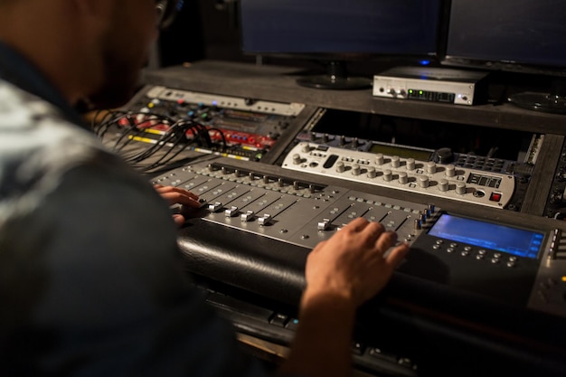 music, technology, people and equipment concept - man using mixing console in sound recording studio