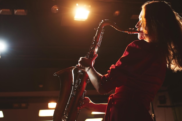 Musician girl in a red dress with a saxophone on stage