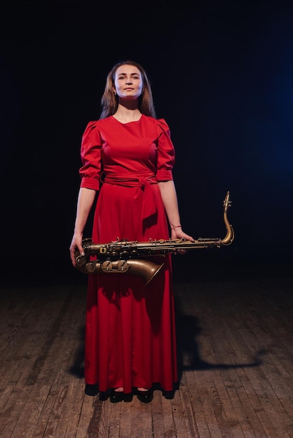 Musician girl in a red dress with a saxophone on stage