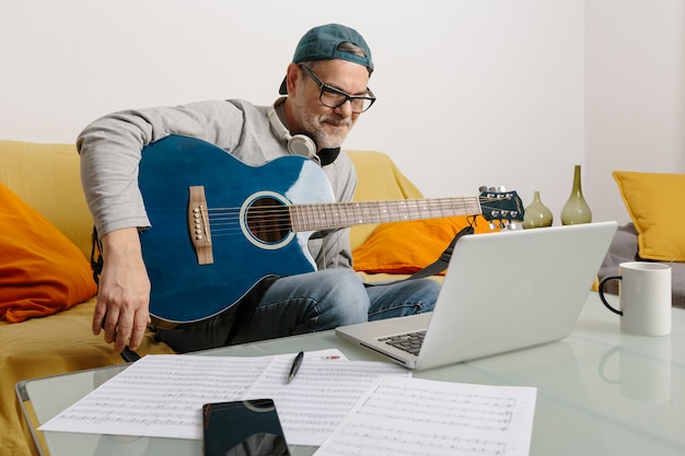 Musician playing the guitar and composing music with his colleagues by video conference through his laptop