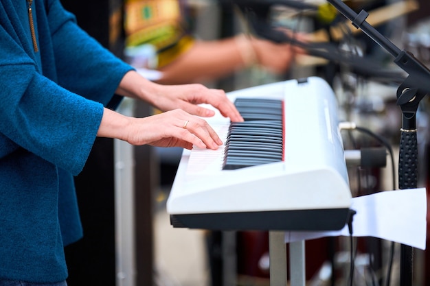 写真 白いシンセサイザーキーボードピアノキーで演奏するミュージシャンの女性は、シンセサイザーの女性の手に焦点を当てます。コンサートステージで楽器を演奏するミュージシャン、シンセサイザーを演奏する人のトリミングされた画像