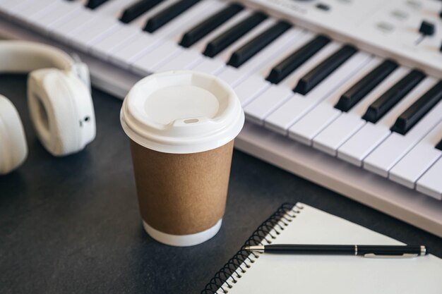 Стол на рабочем месте музыканта с бумажной чашкой и белой клавиатурой фортепиано