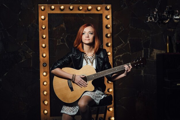 Musician young woman with red hair with an acoustic guitar