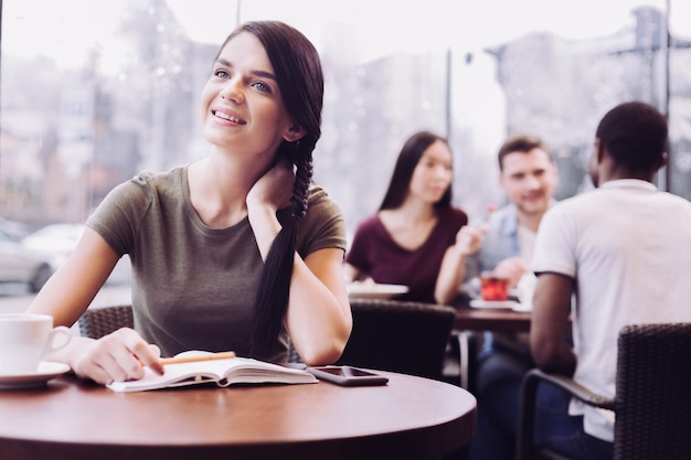 Musing dreamful female student sitting at cafe while staring up and touching her neck