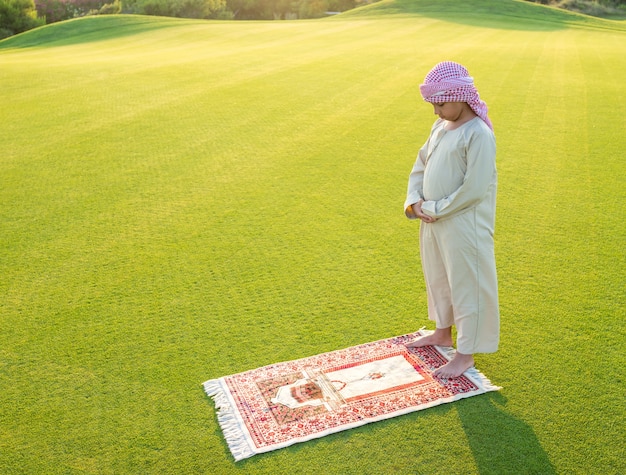 Muslim arabic boy praying on green meadow