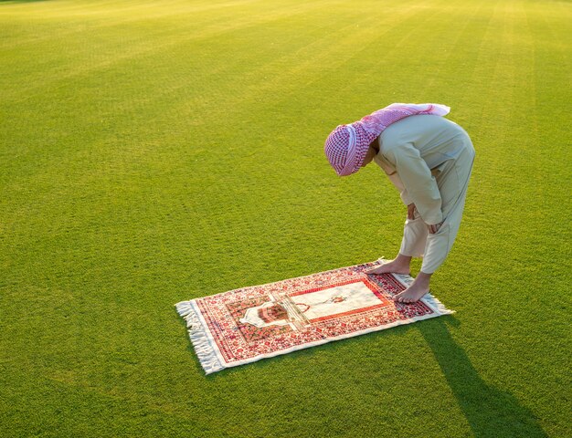 Muslim Arabic boy praying on green meadow