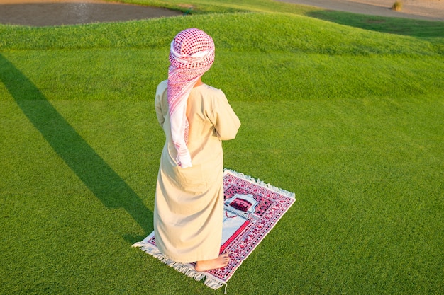 Muslim Arabic boy praying on green meadow