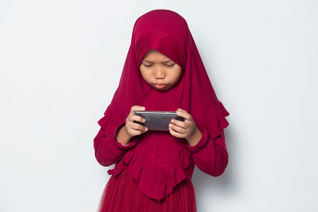 Bambina asiatica musulmana che utilizza il gioco dello smartphone su sfondo bianco