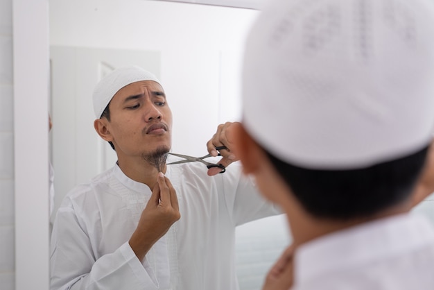 Photo muslim asian man unsure to shave off his beard using scissor