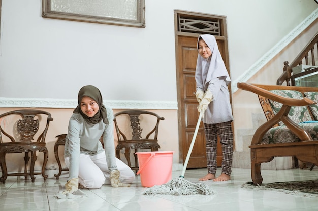 Madre e figlia asiatiche musulmane che sorridono mentre puliscono il pavimento