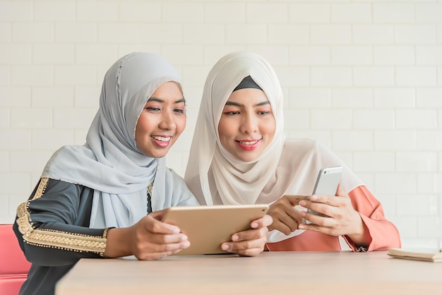 Muslim asian two woman use computer notebook and smart phone in coffee shop or coworking space