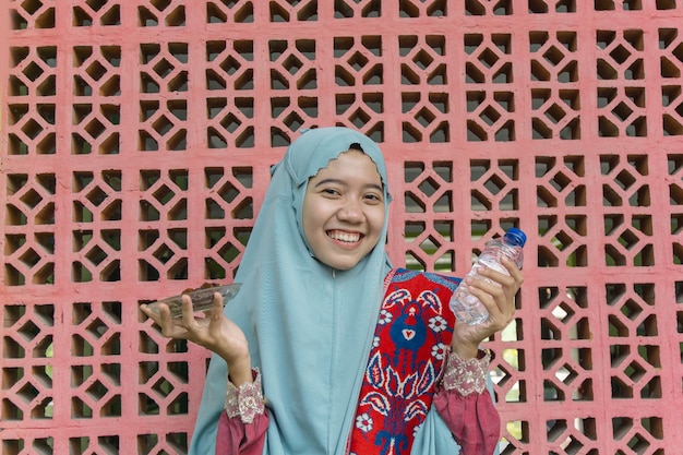 muslim asian woman holding water bottle and plate of dates with islamic ornament background