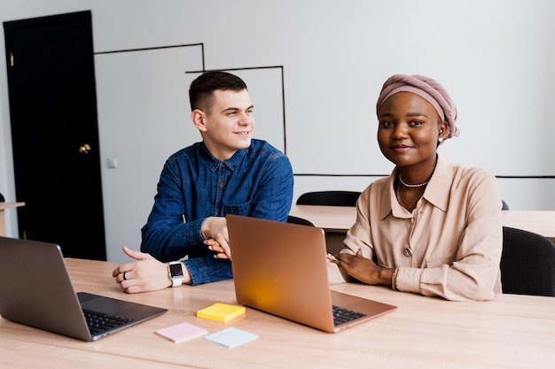 Donna nera musulmana e uomo bianco con il computer portatile. le coppie multietniche lavorano insieme in linea sul progetto di affari.