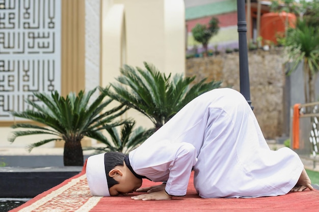 A muslim boarding school student prostrates in the courtyard of\
the mosque