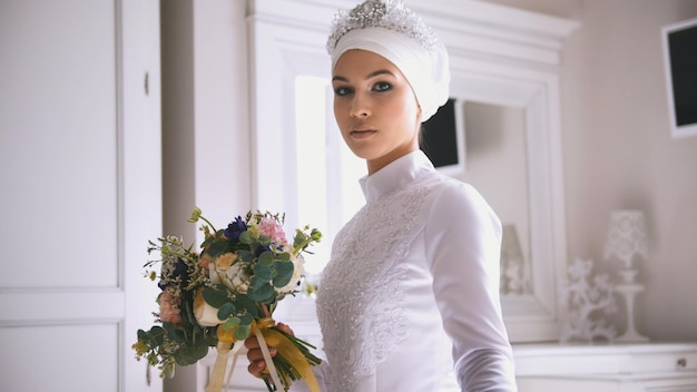 Muslim bride in white wedding dress holding the bouquet of flowers in hand