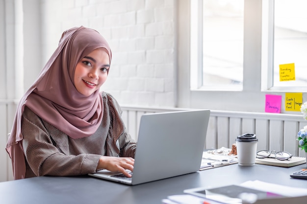 イスラム教徒のビジネス女性茶色のヒジャーブは、事業報告書と電卓とホームオフィスの財務について作業します。