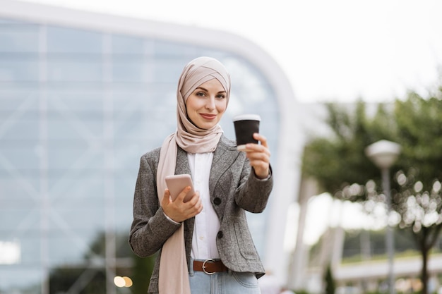 현대적인 건물이나 공항 앞에 서 있는 히잡을 쓴 이슬람 비즈니스 우먼