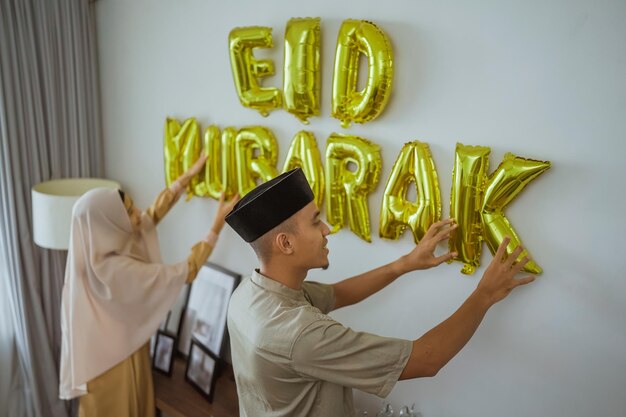 Muslim couple decorating their house with eid mubarak text