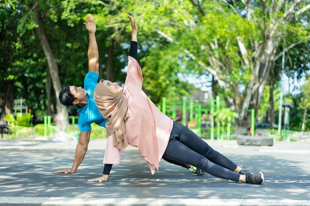 Muslim couple in gym clothes doing hand exercises together in the park