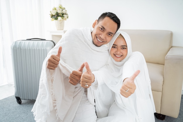 Muslim couple sit wearing white traditional with hands thumb up