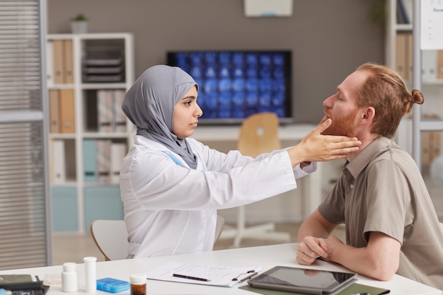 病院での健康診断中にテーブルで患者を診察するイスラム教徒の医師