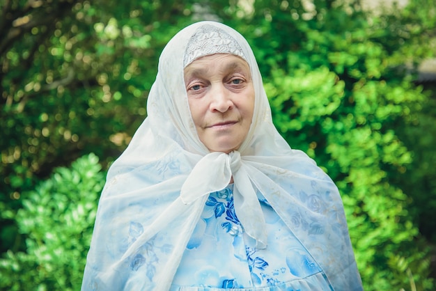 Muslim elderly woman in a white headscarf and a blue dress in the green garden