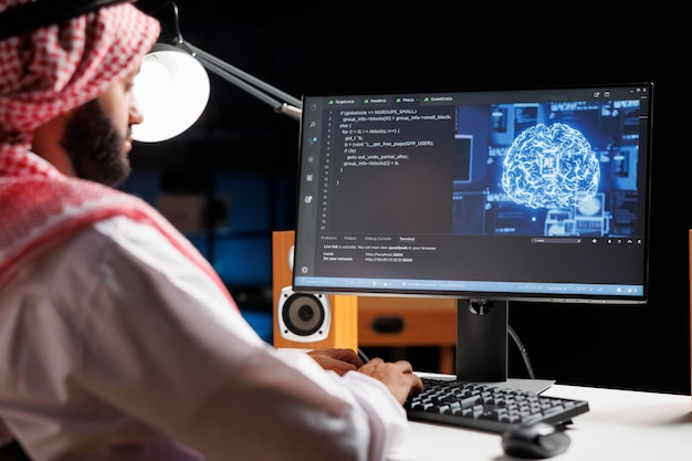 Muslim engineer focuses on a computer screen displaying code and data in a futuristic work setting He manages a robust cloudbased system while monitoring data on a desktop computer screen